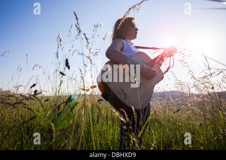 Teenager-Mädchen mit dunkler Brille Gitarre in einer Wiese. Im Freien. Sommer. Stockfoto