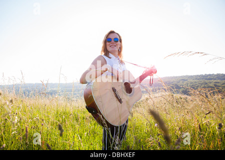 Teenager-Mädchen mit dunkler Brille Gitarre in einer Wiese. Im Freien. Sommer. Stockfoto