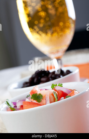 Frische hausgemachte Salsa mit Tomaten, roten Zwiebeln und Koriander, mit eine Schale mit schwarzen Bohnen und ein Bier im Hintergrund. Stockfoto