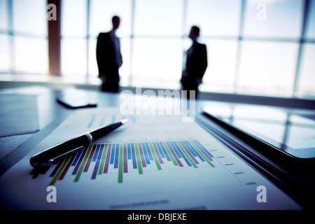 Nahaufnahme von einem Finanzbericht mit den Silhouetten von Geschäftsleuten im Hintergrund Stockfoto