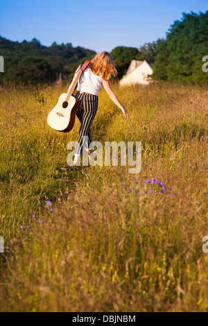 Teenager-Mädchen zu Fuß durch eine Wiese mit einer Gitarre. Im Freien. Sommer. Stockfoto