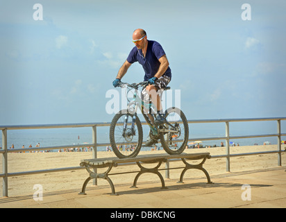 Fahrrad Stunt. Ein Mann mit seinem Fahrrad über eine Bank, auf der Promenade in Brighton Beach in Brooklyn, New York v Stockfoto