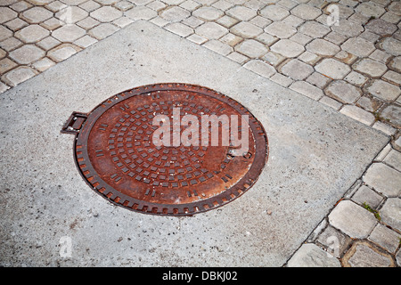 Alte verrostete Kanalisation Kanaldeckel auf der gepflasterten Straße Stockfoto