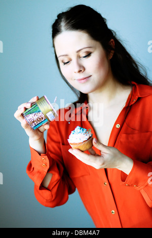 Frau im roten Kleid legt Belag auf Cupcake, Kopenhagen, Dänemark Stockfoto