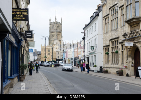 Geschäfte auf Dyer Street in Cirencester mit St John The Baptist Church im Hintergrund Stockfoto