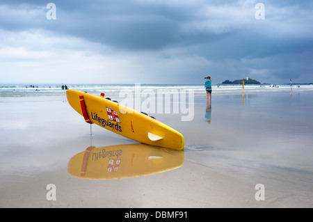 RNLI Rettungsschwimmer Paddle Board auf Gwithian Beach, North Cornwall. Ein Fotograf fotografiert Surfer im Meer hinter. Bild von Julie Edwards Stockfoto