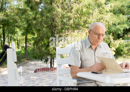 Mann liest ein Menü in einem open-air-Café sitzen an einem Tisch im Schatten eines Baumes Stockfoto