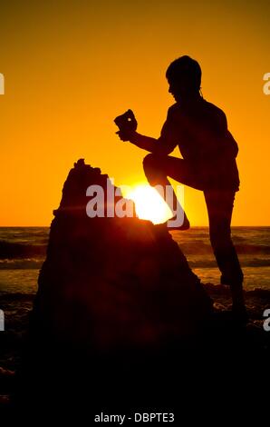 Einen jungen hält ein Addierer Stein (Firestone mit einem Loch) bis die Sonne an der Nordsee bei Sonnenuntergang an der Westküste in Agger, Dänemark, 16. Juli 2013. Foto: Patrick Pleul Stockfoto