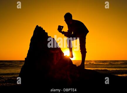 Einen jungen hält ein Addierer Stein (Firestone mit einem Loch) bis die Sonne an der Nordsee bei Sonnenuntergang an der Westküste in Agger, Dänemark, 16. Juli 2013. Foto: Patrick Pleul Stockfoto