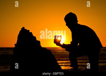 Einen jungen hält ein Addierer Stein (Firestone mit einem Loch) bis die Sonne an der Nordsee bei Sonnenuntergang an der Westküste in Agger, Dänemark, 16. Juli 2013. Foto: Patrick Pleul Stockfoto