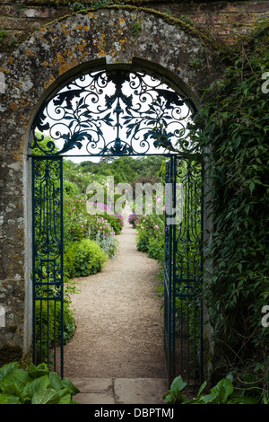 Blick auf den ummauerten Garten von rousham House im Sommer durch die blauen verzierten schmiedeeisernen Tor in einem Cotswold - steinernen Torbogen, Oxfordshire, England. Stockfoto