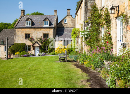 Honig-gesteinigt Cotswold Hütten mit Rosen und Sommerblumen, neben den Dorfanger in Stanton, Gloucestershire, England Stockfoto