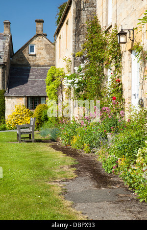 Honig-gesteinigt Cotswold Hütten mit Rosen und Sommerblumen, neben den Dorfanger in Stanton, Cotswolds, Gloucestershire, England Stockfoto