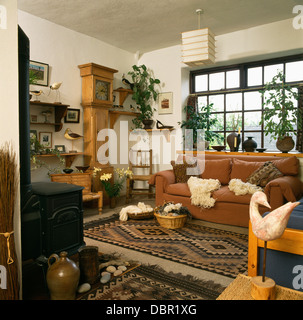 Körbe aus Wolle und gemusterten Teppich in Wirtschaft-Stil Wohnzimmer mit Kiefer lange Fall Uhr und Holzofen Stockfoto