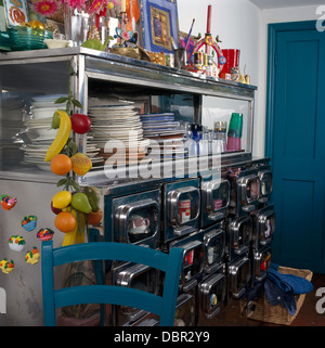 Stapel von Platten auf 50er Jahre Metall-Kommode mit Schubladen und dekoriert mit Kunststoff Obst Garland in kleinen, Retro-Küche Stockfoto