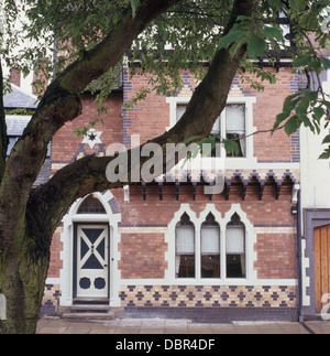 Baum neben viktorianischen Reihenhaus Ziegel Hütte mit gotischen Fenstern Stockfoto