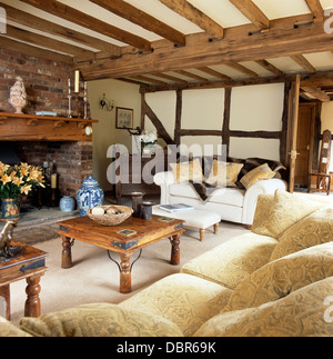 Bequemen Sofas Creme und indonesischen Couchtische im Land Wohnzimmer mit rustikalen Holzbalken Stockfoto