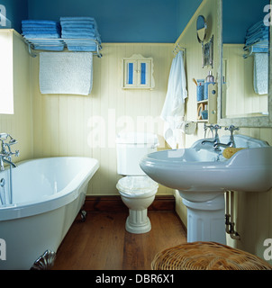Kralle-Fussbad im blauen Badezimmer mit blauen Tüchern auf Chrom Regal an weiße Zunge + Nut getäfelten Wand Stockfoto