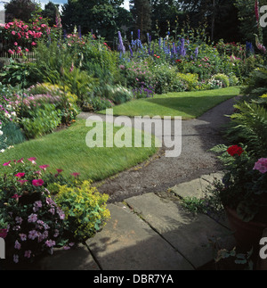 Rosa Petunien in Topf neben Weg und neu gemäht im Sommergarten mit breiten Rand von Rittersporn und rosa Rosen Stockfoto