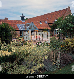 Sträucher in Grenze des Gartens vor umgebaute Scheune mit Glas-Veranda-Erweiterung Stockfoto