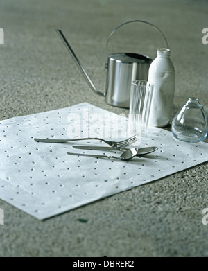 Nahaufnahme von kleinen Edelstahl-Olivenöl gießen kann und Besteck auf weiße Matte mit Glasvasen Stockfoto