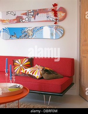 Zwei Skateboards an Wand über rotes Sofa mit bunten Kissen in modernen weißen Wohnzimmer Stockfoto