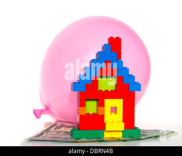 Modellhaus von herkömmlichen Legosteinen ruht auf Dollarnoten und stützte sich auf einen rosa Bubble-Ballon auf weißem Hintergrund Stockfoto