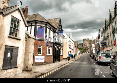 Geschäfte auf Castle Street, einer der Hauptstraßen von Conwy, die parallel zum Meer verläuft. Conwy ist eine historische Festungsstadt am bekanntesten für Conwy Castle, das steht am südlichen Ende der Castle Street und ist sichtbar in der Mitte-rechts des Rahmens. Stockfoto