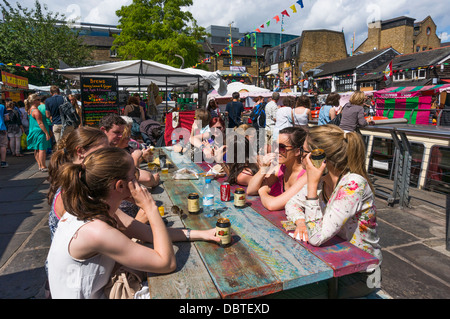 Menschen, die auf Essen und Trinken Tisch in Camden Market, London, England, UK. Stockfoto