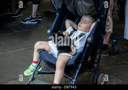 Ein junger weißer Junge schlafend in seinem Buggy mit Kuscheltier auf seinem Schoß, im Camden Market, London, England, UK. Stockfoto