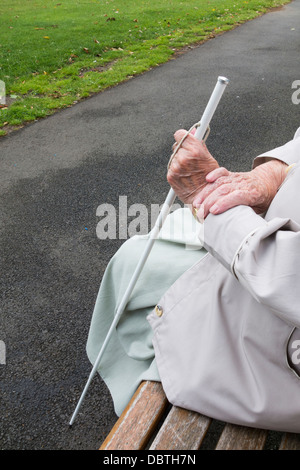 Neunzig Jahre alte Sehbehinderte Dame mit weißen Stock sitzen auf Bank im öffentlichen Park. England, UK Stockfoto