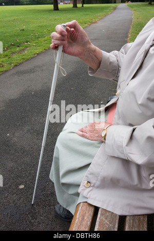 Neunzig Jahre alte Sehbehinderte Dame mit weißen Stock sitzen auf Bank im öffentlichen Park. England, UK Stockfoto