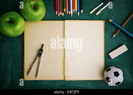 Aufgeschlagene Buch und die Schule-Versorgungsmaterialien, Tafel im Hintergrund. Stockfoto