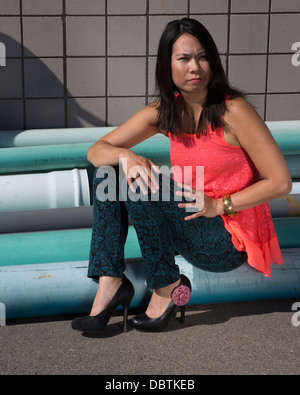 Modische Frau, die sich zum Ausgehen verkleidet hat und auf Industriepfeifen sitzt Stockfoto