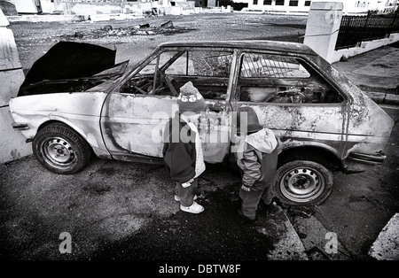 Kinder spielen in der Nähe von einem ausgebrannten Auto in Devonport, England. Anfang der neunziger Jahre Bild. Stockfoto