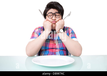 Besorgt übergewichtiger junge Mann Blick auf leeren Teller Stockfoto