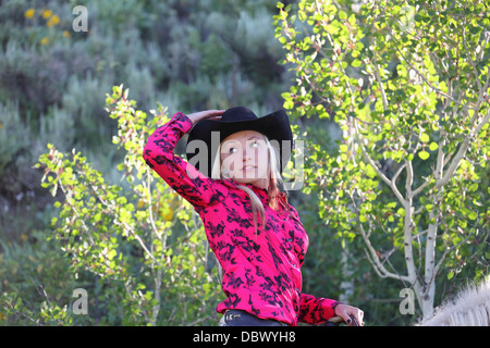 hübsches Cowgirl auf dem Pferderücken in Montana Ranch gegen beleuchtete Bäume Stockfoto