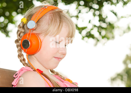 Mädchen sitzen auf der Bank im Park und hören audio Sprachkurs über weiße und grüne Bokeh Hintergrund Stockfoto