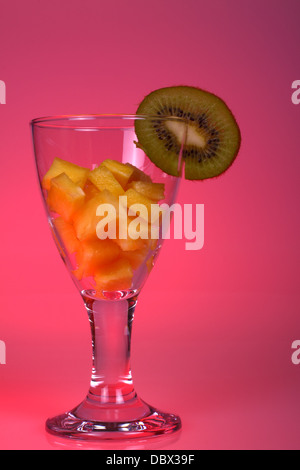 Glas mit gewürfelter Ananas und Kiwi mit einem rosa Hintergrund Stockfoto