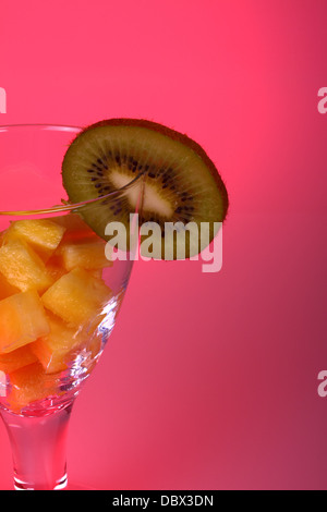 Glas mit gewürfelter Ananas und Kiwi mit einem rosa Hintergrund Stockfoto