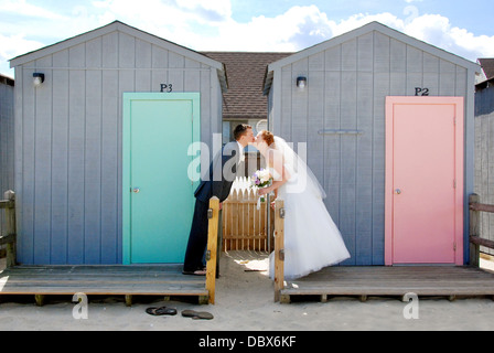 Ein Brautpaar Braut und Bräutigam küssen vor blau und rosa Cabanas am Strand von Jersey Shore Strandhochzeit Stockfoto