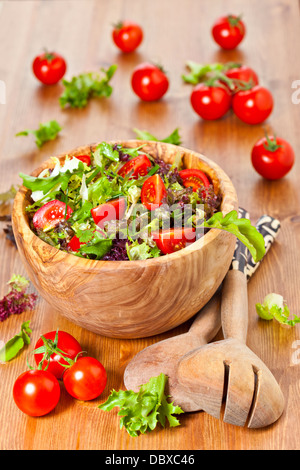 Schale aus Olivenholz gefüllt mit gemischten Blattsalat und Cherry strauchtomaten auf Holztisch Stockfoto