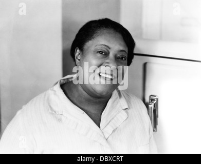 1930S 1940S PORTRAIT LÄCHELND AFROAMERIKANISCHE FRAU INLÄNDISCHEN DURCH KÜHLSCHRANK KÜCHE MIT BLICK IN DIE KAMERA Stockfoto