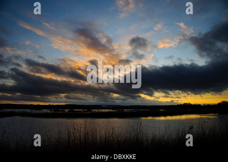 Das Nachleuchten zu beleuchten, die Wolken mit gelb und Orange über den Röhrichten und Lagunen der Somerset Levels Stockfoto