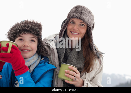 Glückliche Mutter und Sohn in Pelzmützen trinken heiße Schokolade Stockfoto