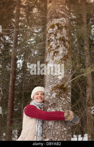 Glückliche Frau umarmt Baumstamm im Wald Stockfoto