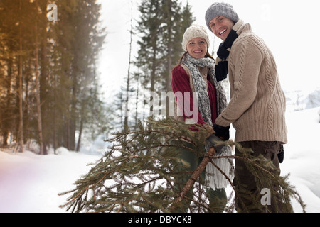 Porträt des glücklichen Paares mit frischen Weihnachtsbaum im verschneiten Wald Stockfoto