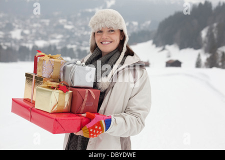 Porträt der lächelnde Frau, die Weihnachtsgeschenke in schneebedecktes Feld Stockfoto