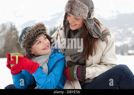 Glückliche Mutter und Sohn trinken heiße Schokolade in schneebedecktes Feld Stockfoto