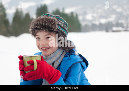 Fröhlicher junge heiße Trinkschokolade in schneebedecktes Feld Stockfoto